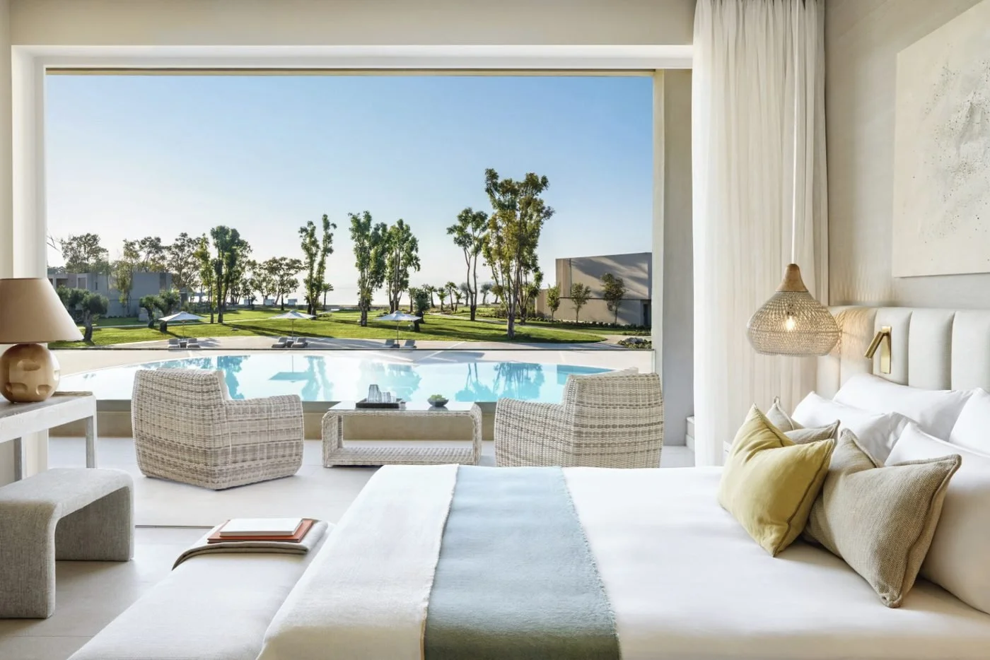 A One Bedroom Bungalow Suite bedroom opening onto a balcony with armchairs above a pool and gardens