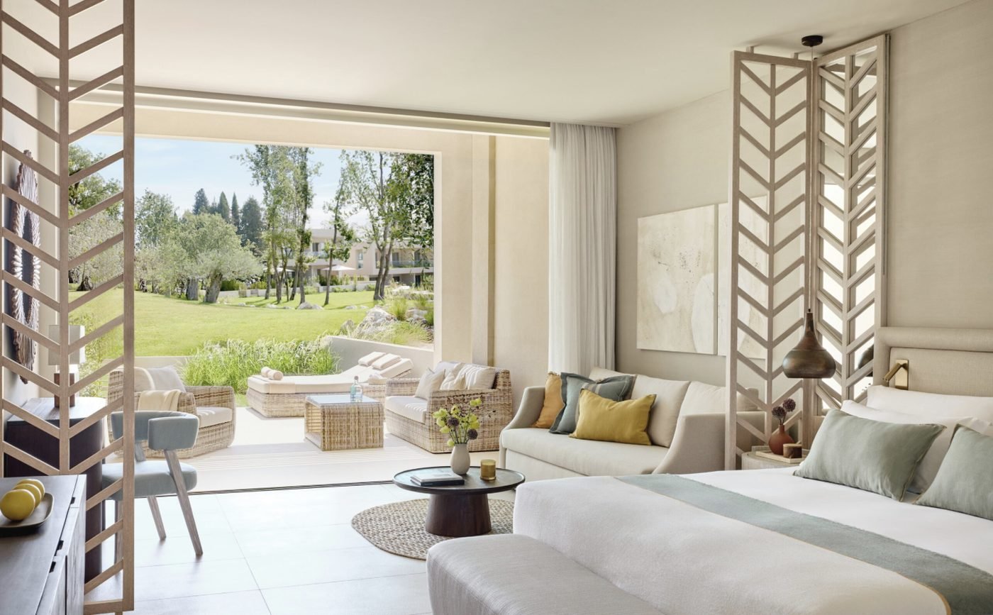 A Deluxe Junior Bungalow Suite with a sofa and bed facing a terrace with loungers and a lawn