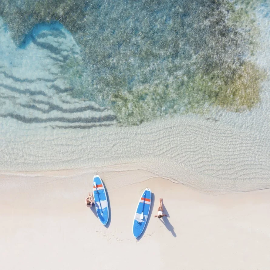 Two paddleboards on white sand beside clear water