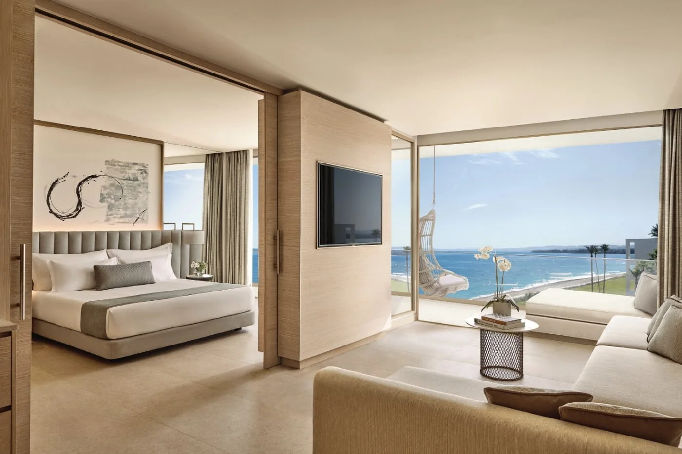 A Deluxe One Bedroom Suite with a bedroom behind sliding doors and a living room opening onto a balcony above the beach