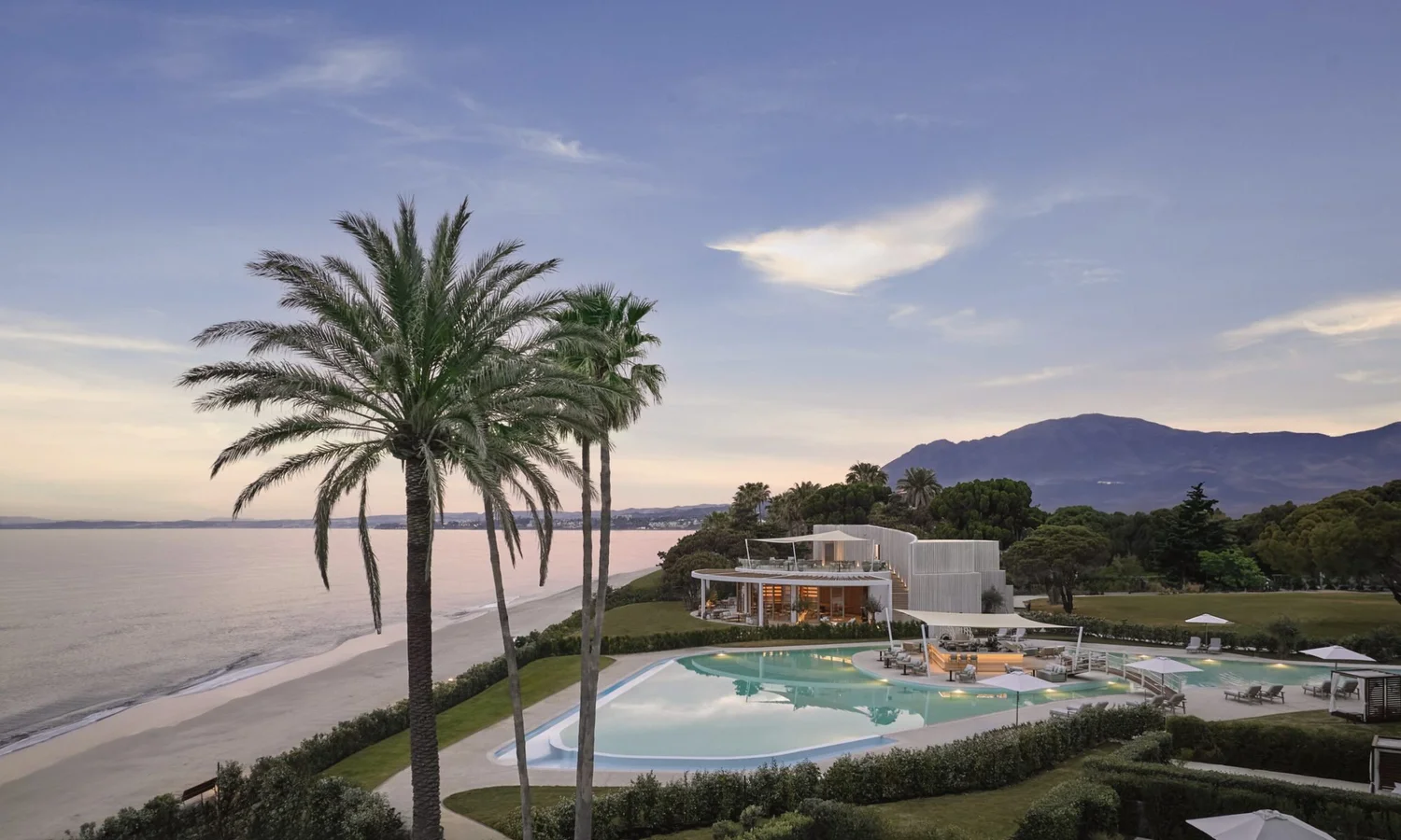 The resort at dusk with palms, pools and mountains