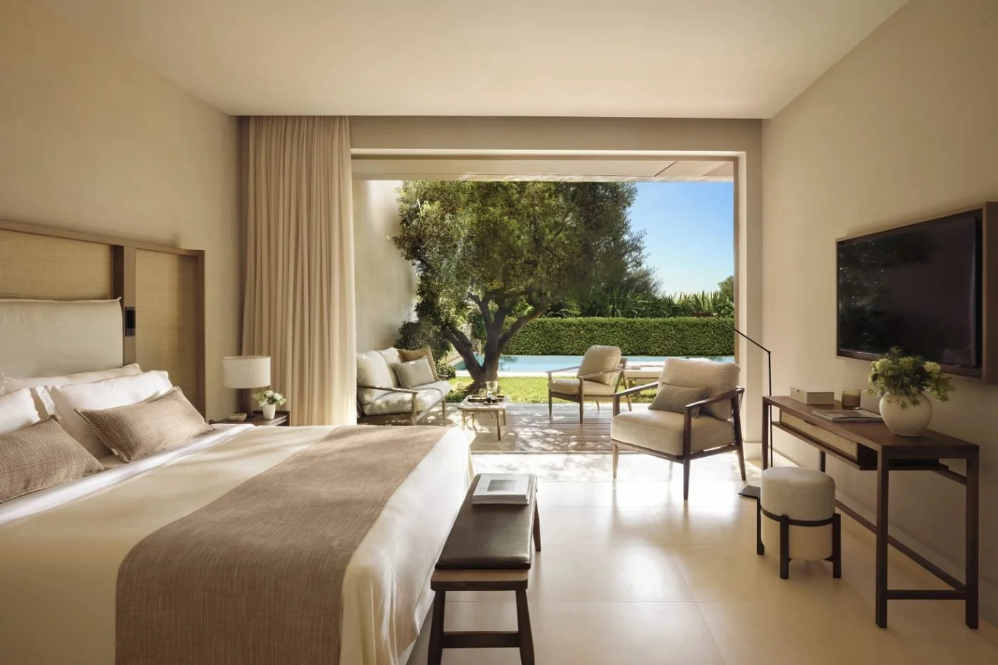 Bedroom of a One Bedroom Bungalow Suite at Sani Club opening onto a terrace, an olive tree and the private pool