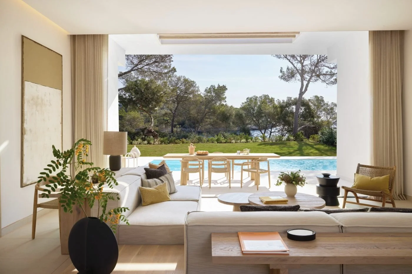 The lounge of a Deluxe Three Bedroom Residence opening onto a private pool, a lawn and pines by the sea