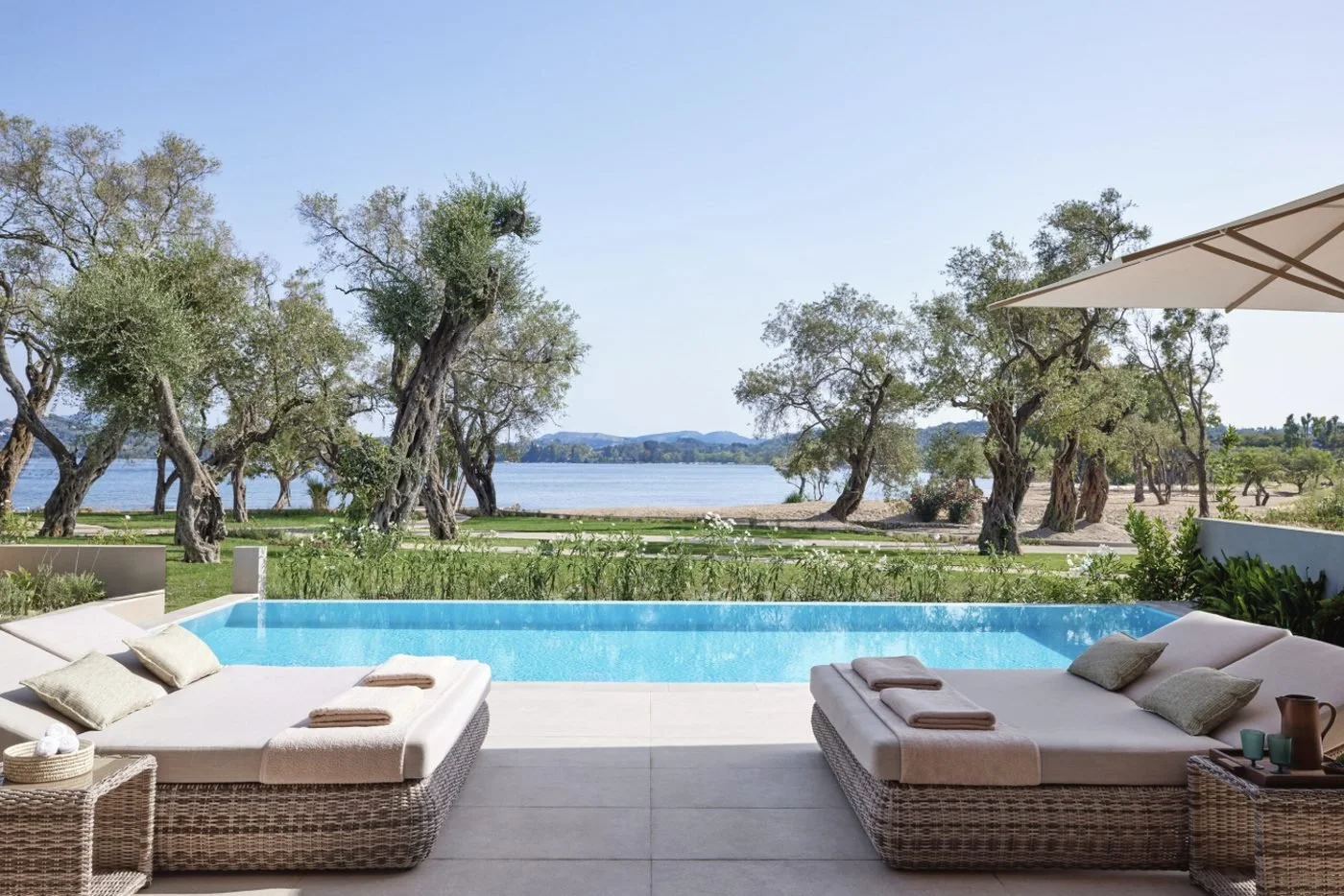 Two daybeds beside the private pool of a Deluxe Two Bedroom Bungalow Suite, with olive trees and the bay beyond