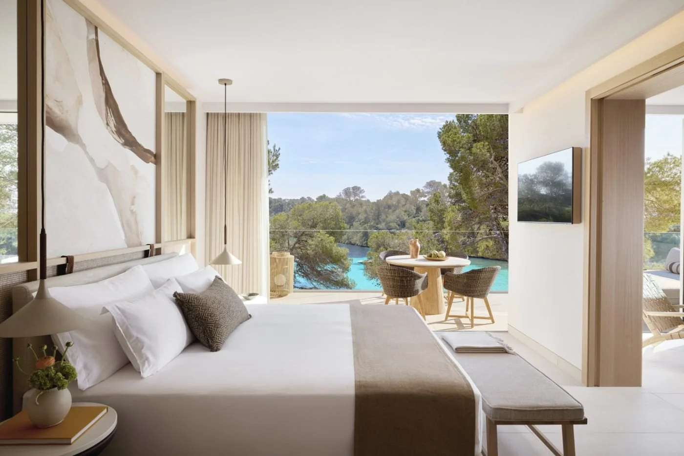 The bedroom of a Deluxe One Bedroom Suite opening onto a balcony above a turquoise cove