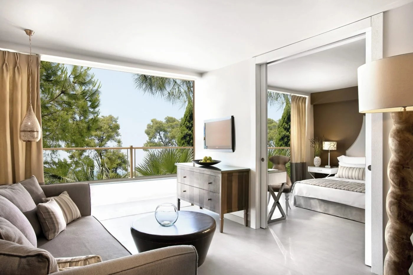 The living room of a One Bedroom Family Suite Garden View looking out to pine trees, with the bedroom beyond