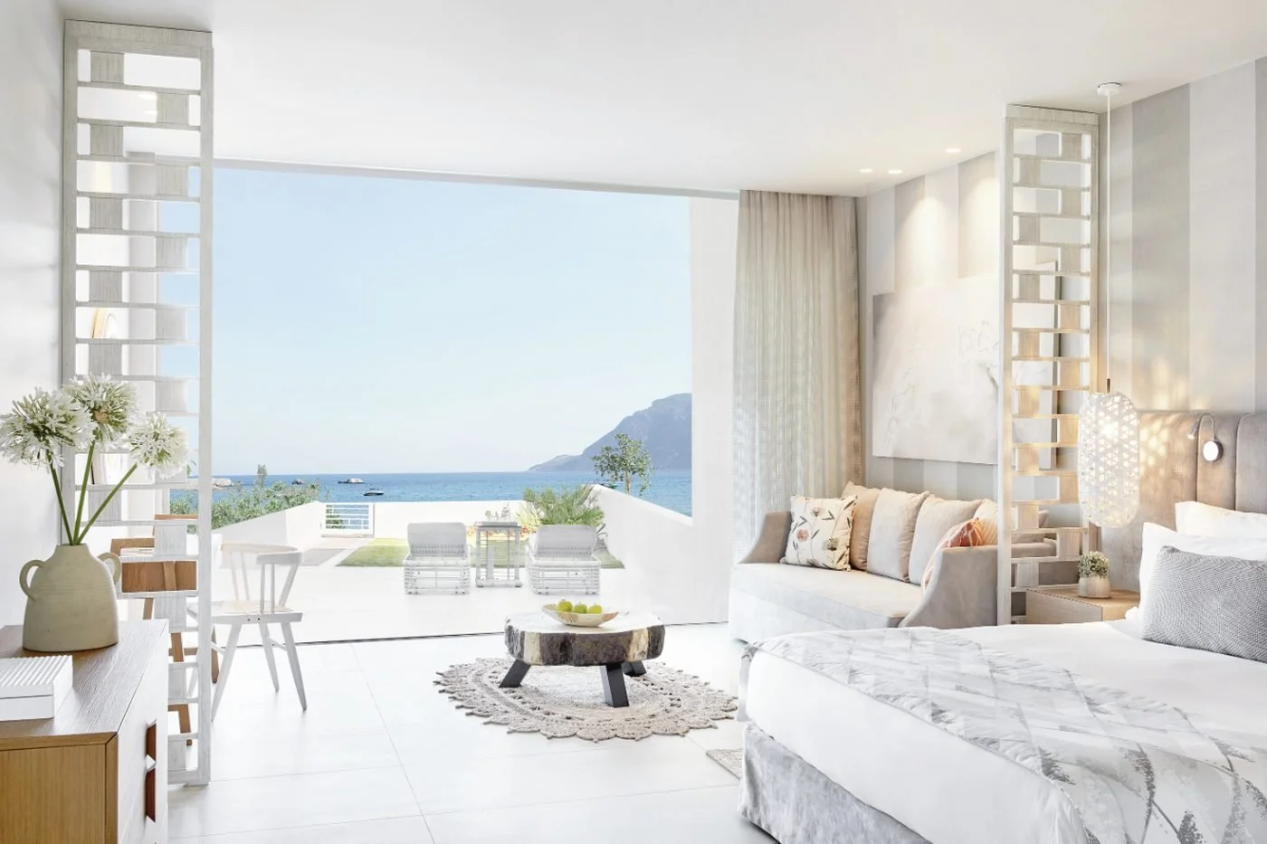 A Deluxe Junior Suite Private Garden at Ikos Aria opening onto a terrace and garden with the sea and mountains beyond