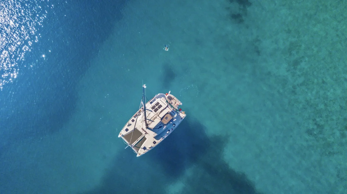 A catamaran at anchor in clear turquoise water, seen from above