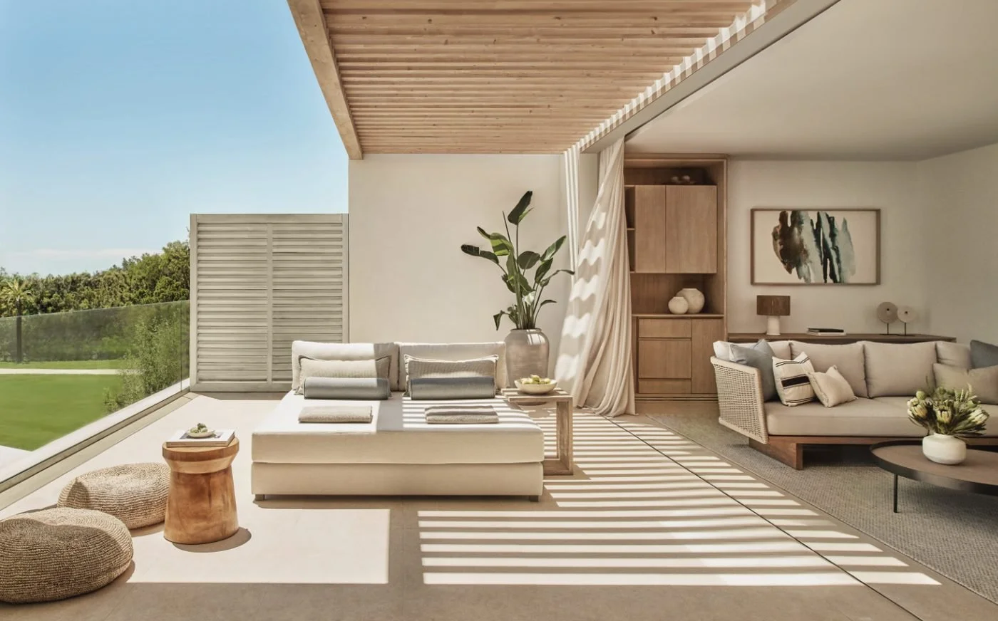 The covered terrace of a Deluxe One Bedroom Penthouse Suite, with a daybed in dappled shade and a living room beyond