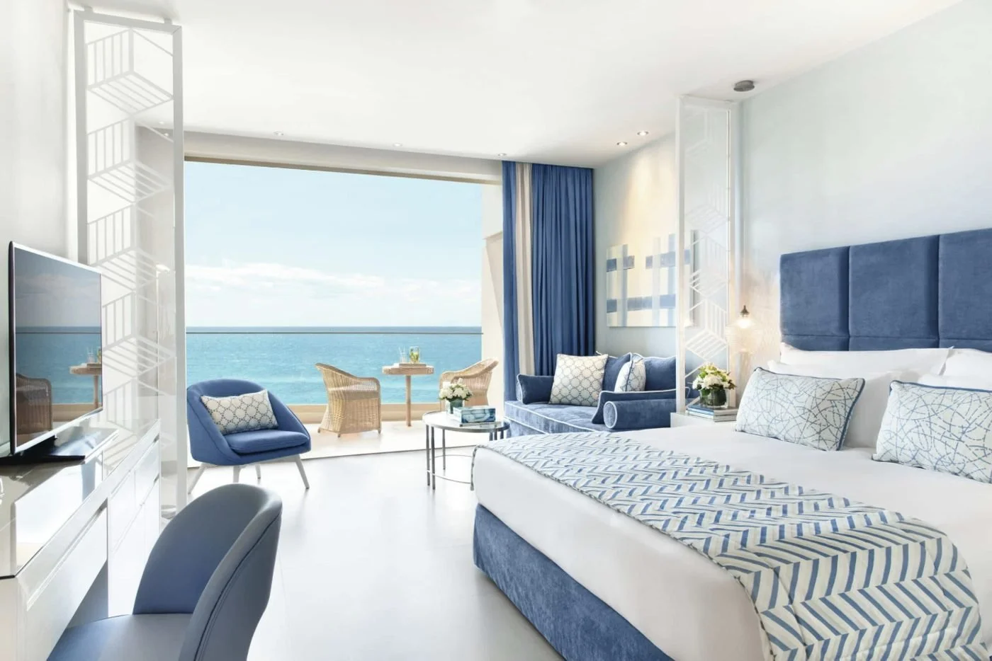 An open-plan Junior Suite at Ikos Oceania with a sofa area and a terrace facing the sea