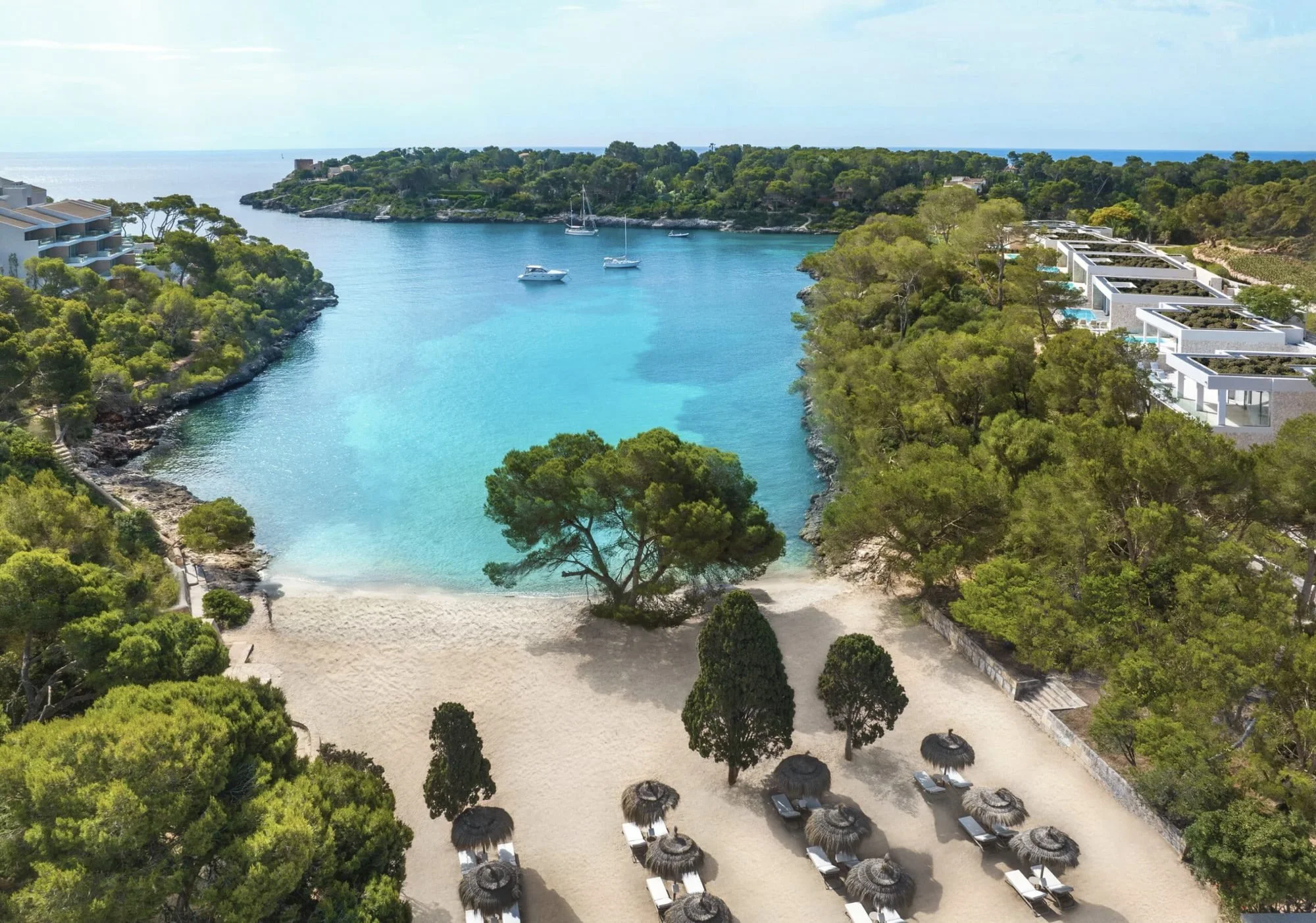 A sheltered turquoise cove at Ikos Porto Petro, with a sandy beach, thatched parasols and suites among the pines