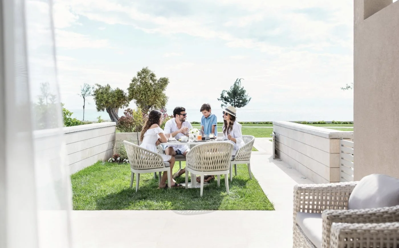 A family having breakfast on the garden terrace of a beach front family suite at Sani Dunes, with the sea beyond