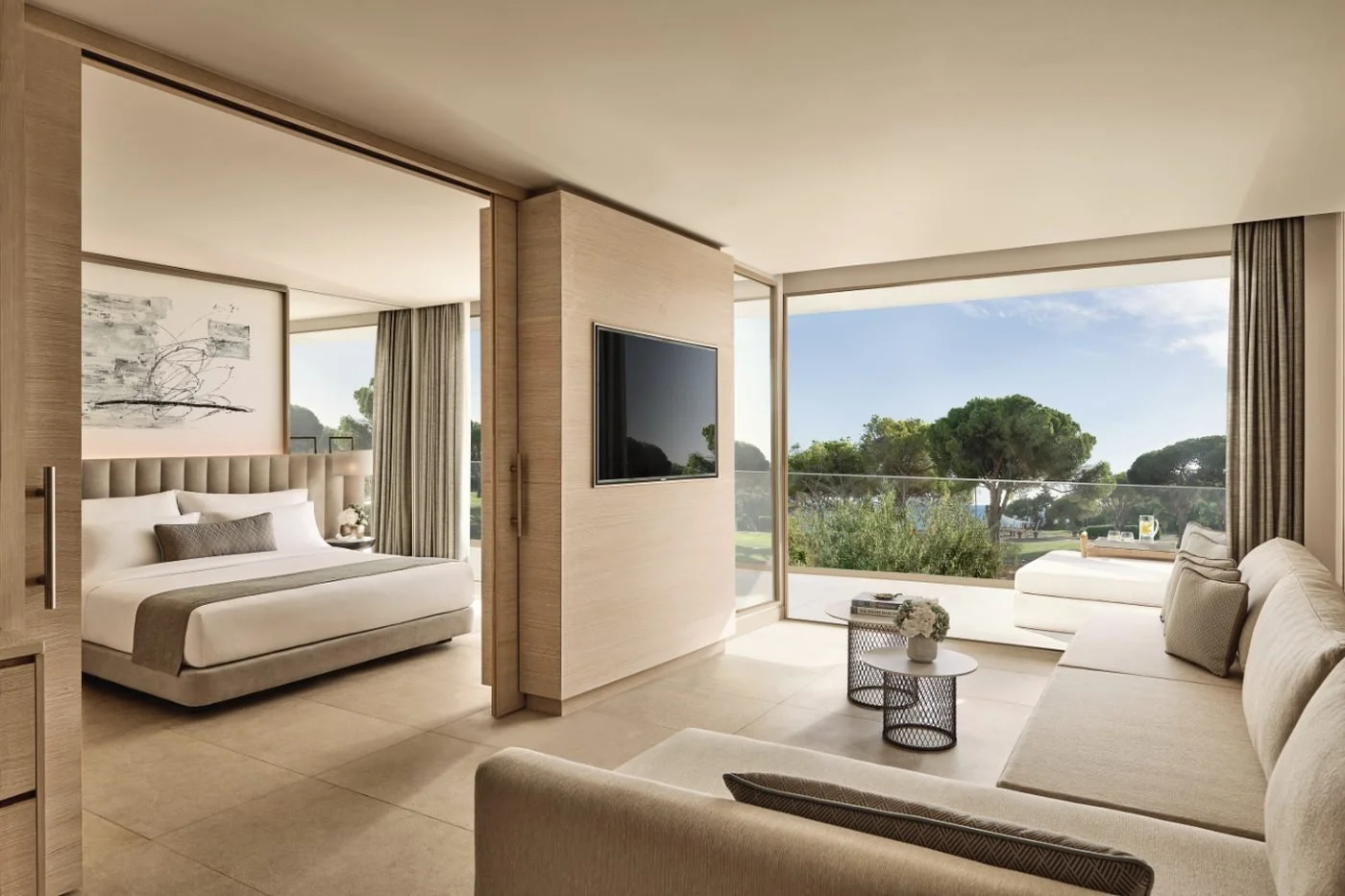 A One Bedroom Suite at Ikos Andalusia with the bedroom behind sliding doors and a living room opening onto a balcony and pine trees
