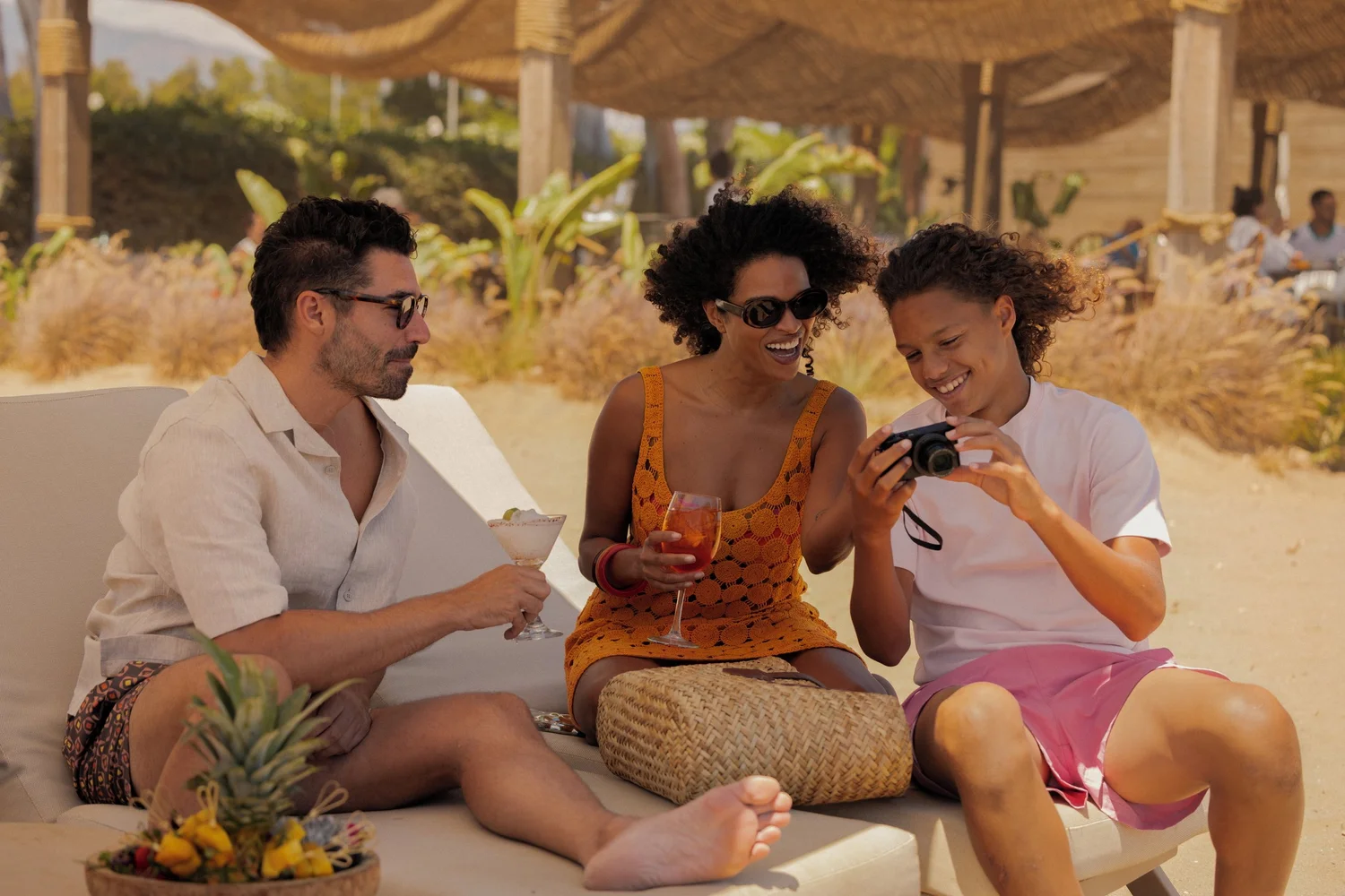 A family sharing drinks and holiday photos on a shaded beach bed at Ikos Andalusia