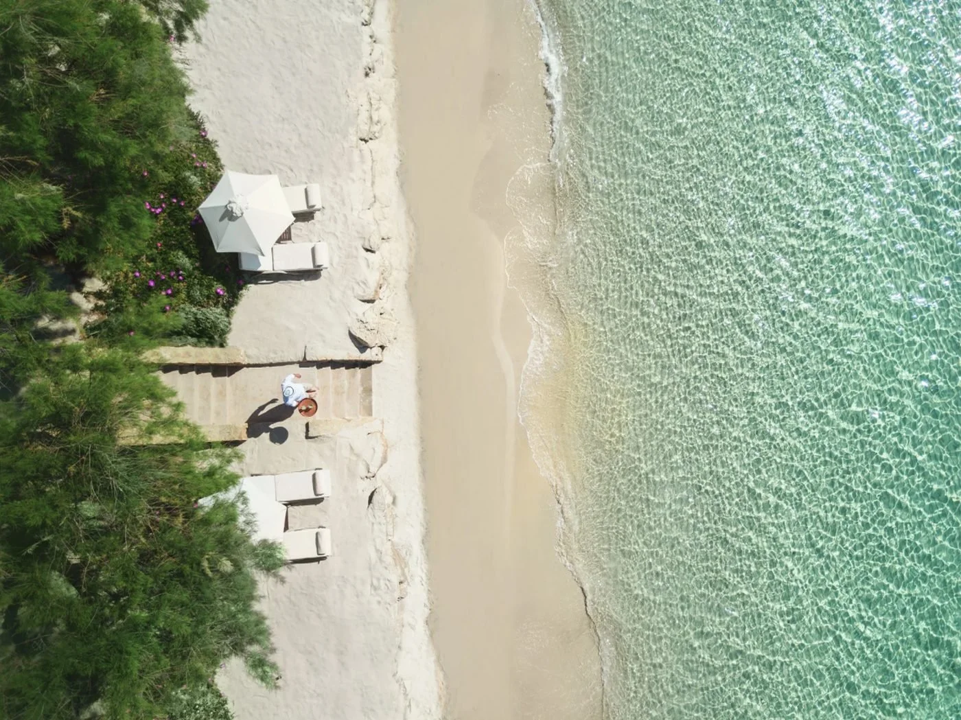 Looking down on Sani Club's white sand beach, with a waiter carrying a tray down to the sun loungers