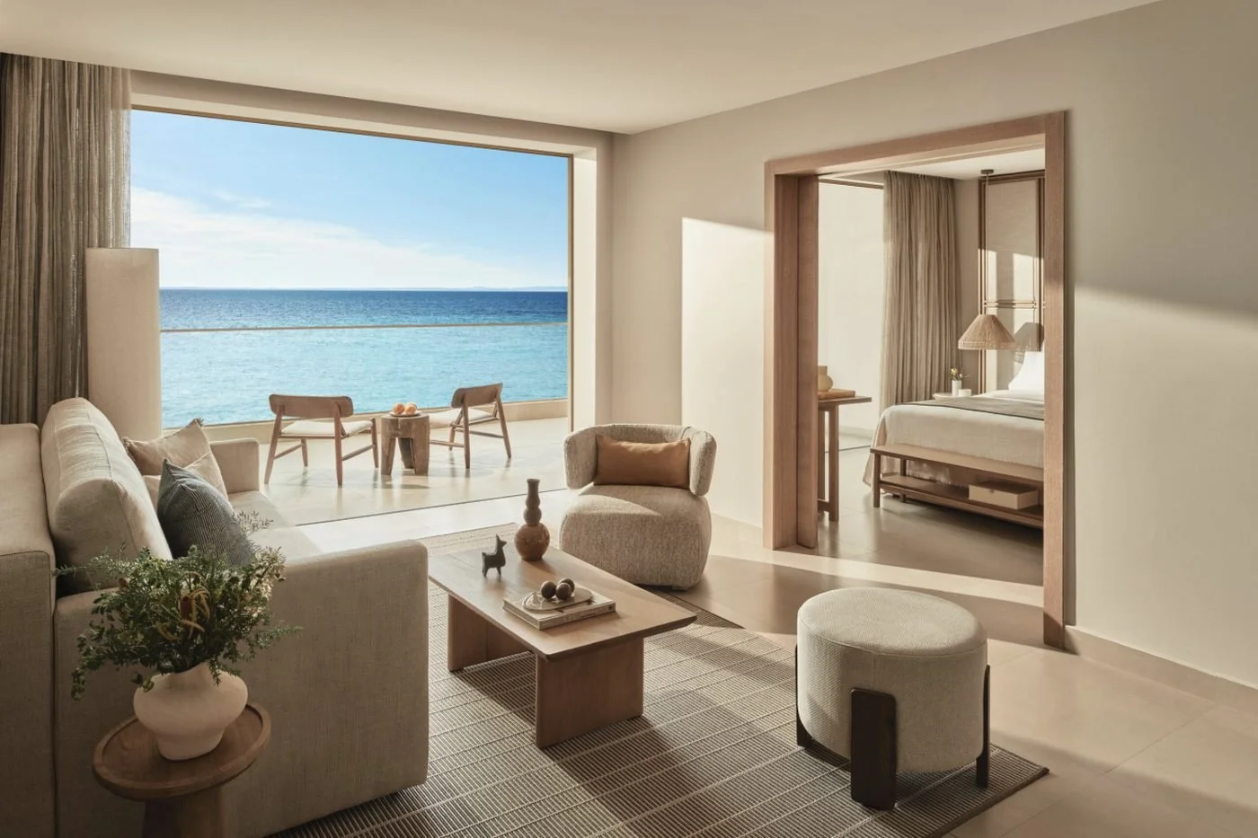 The living room of a beachfront Deluxe suite at Ikos Olivia, with wide glass doors open to its balcony and the sea