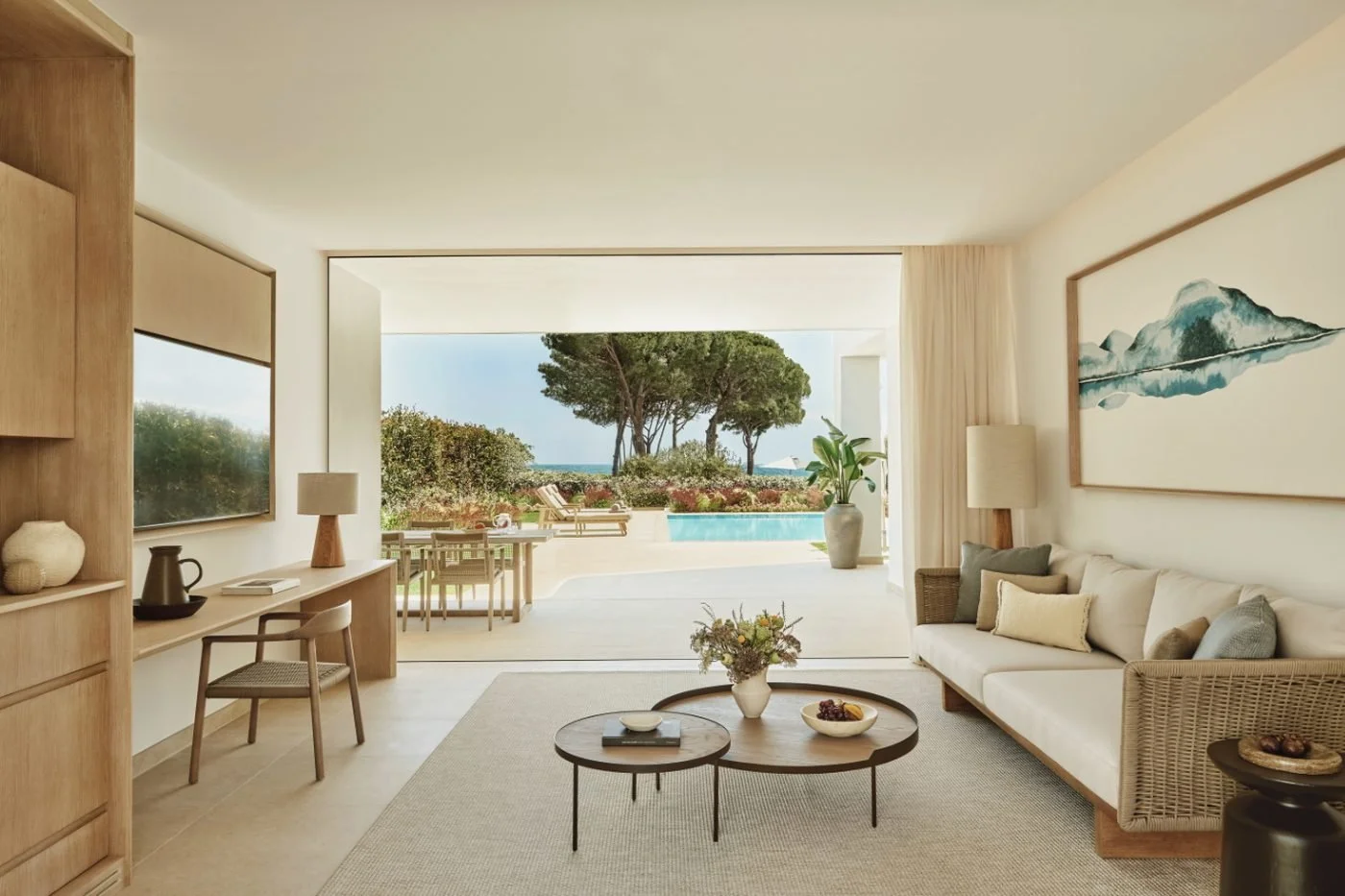 The living room of a Deluxe Three Bedroom Suite opening onto a terrace with a dining table, a private pool and pine trees