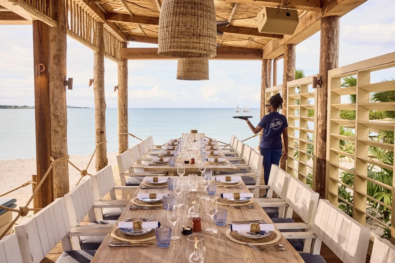 A long table set for lunch at The Hut beach club, open to the sea
