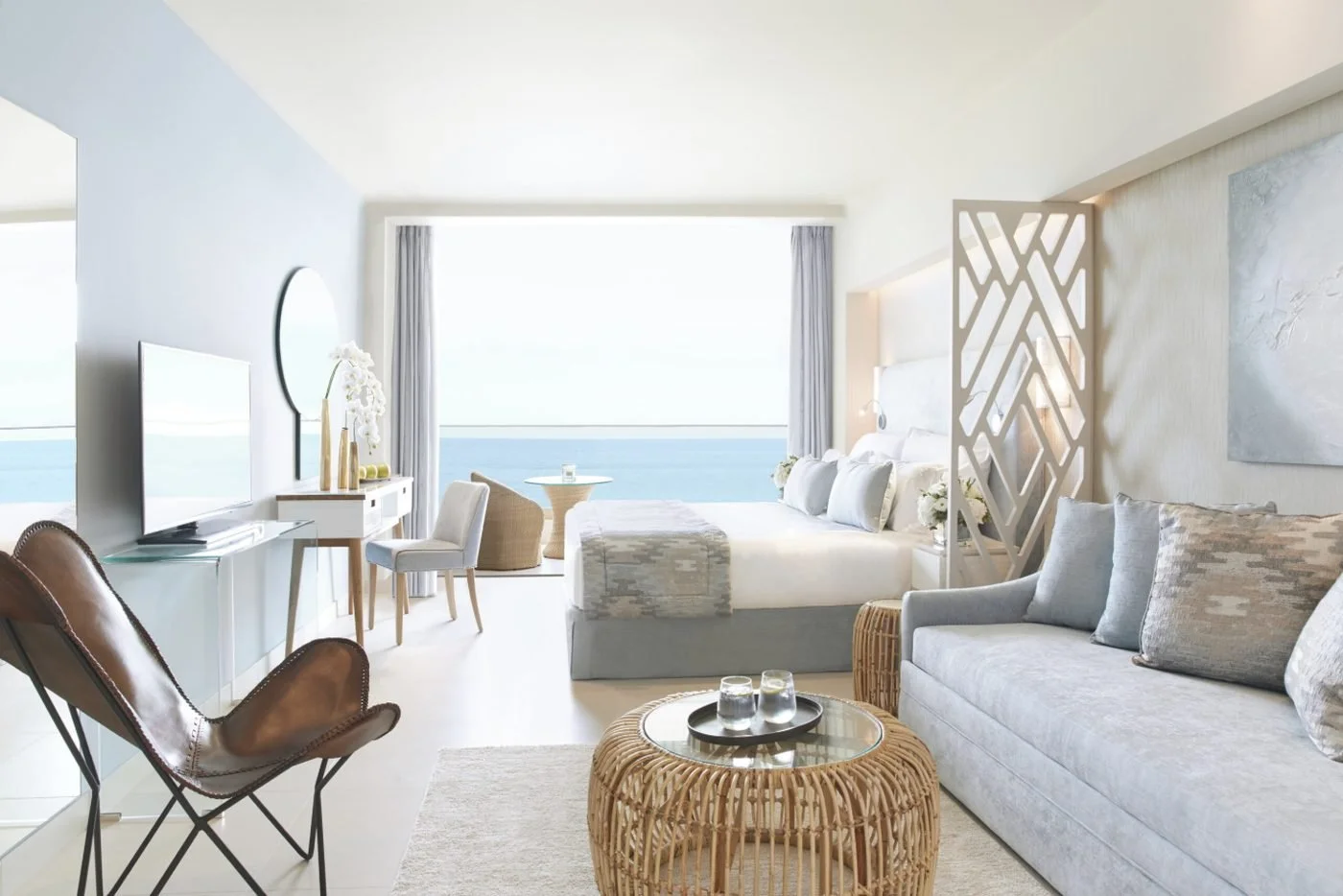 An open-plan Junior Suite with a sofa, armchair and bed, and the sea beyond the balcony