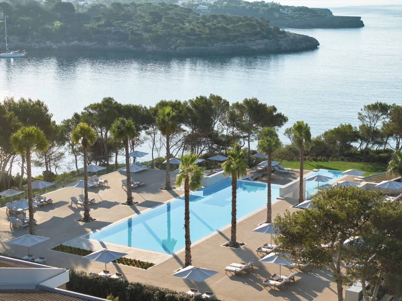 A long infinity pool lined with palms and parasols above a calm bay