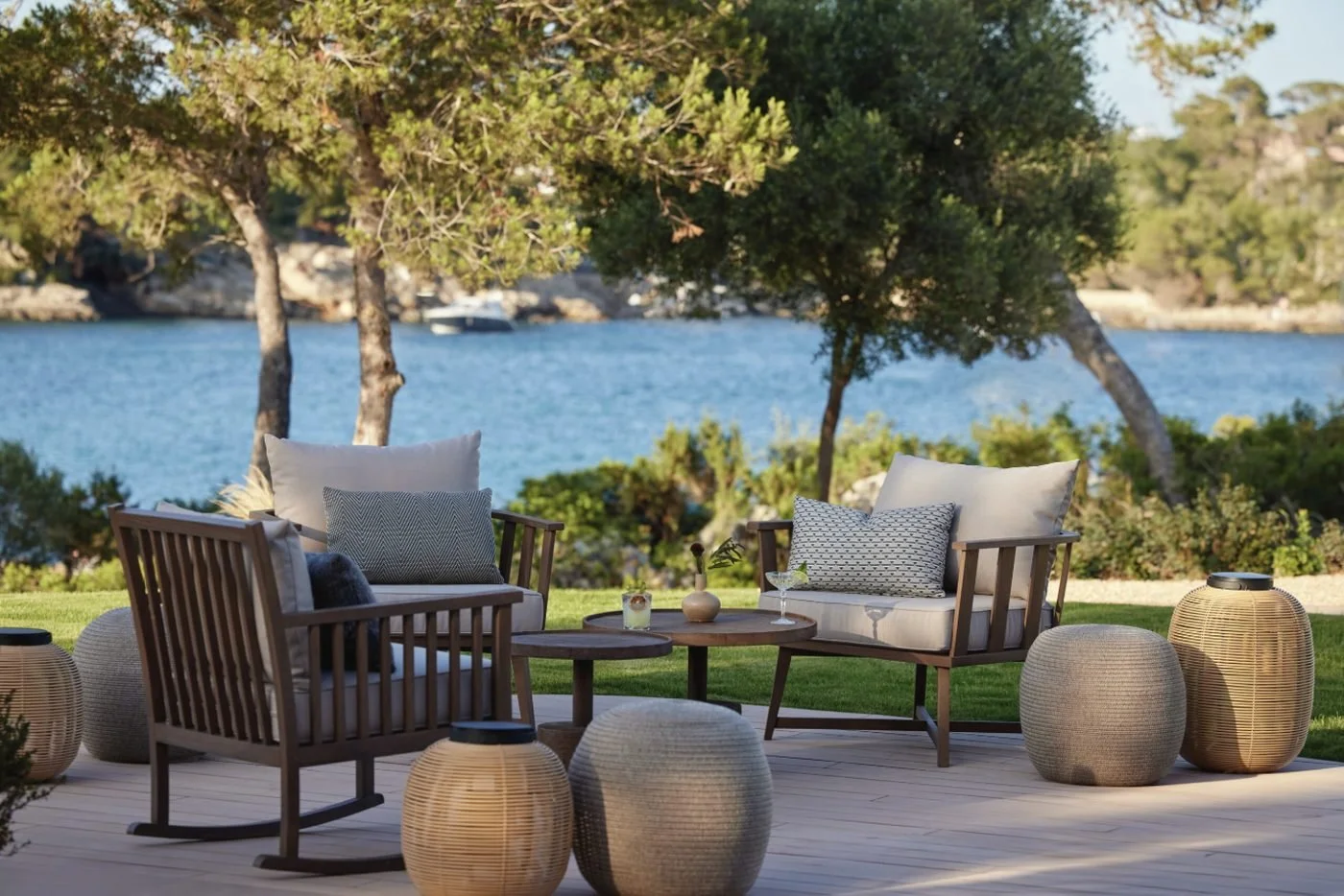 Armchairs and lanterns on a lawn terrace under the pines, looking across the bay