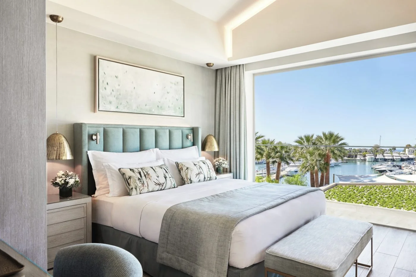 The bedroom of a Deluxe One Bedroom Suite with a wide window over palm trees and yachts in Sani Marina