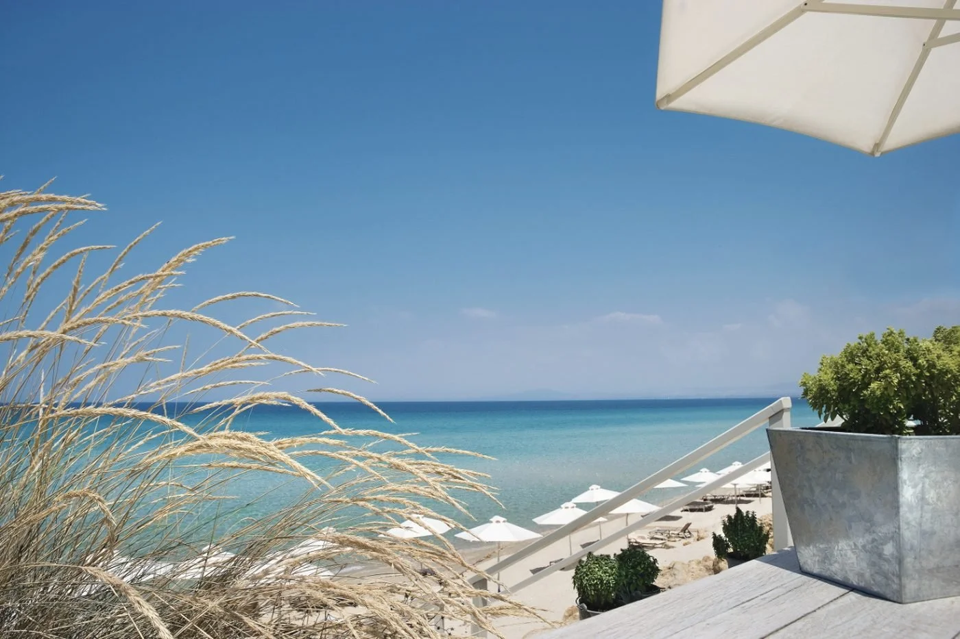 The view from the deck at Bousoulas Beach Bar over swaying grasses to parasols on the sand and a turquoise sea