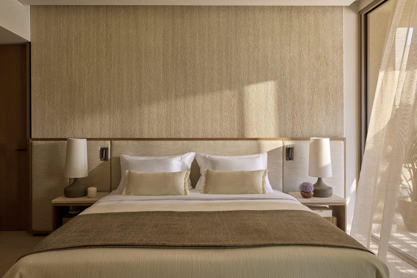 A calm bedroom in natural tones at Sani Asterias, with a textured wall and sheer curtains