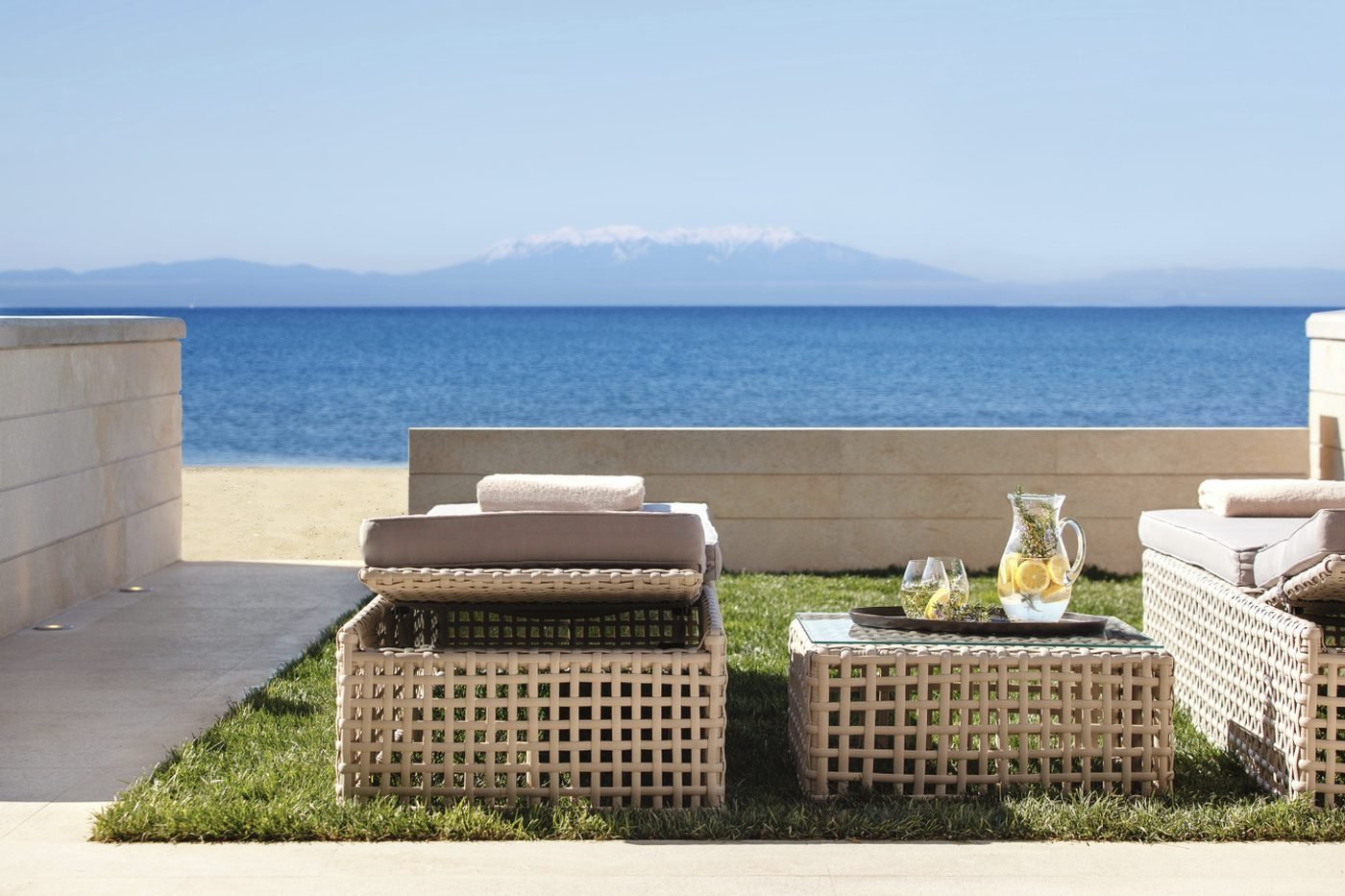 The garden terrace of a beach front suite at Sani Dunes, with loungers on the lawn and the sea and mountains beyond