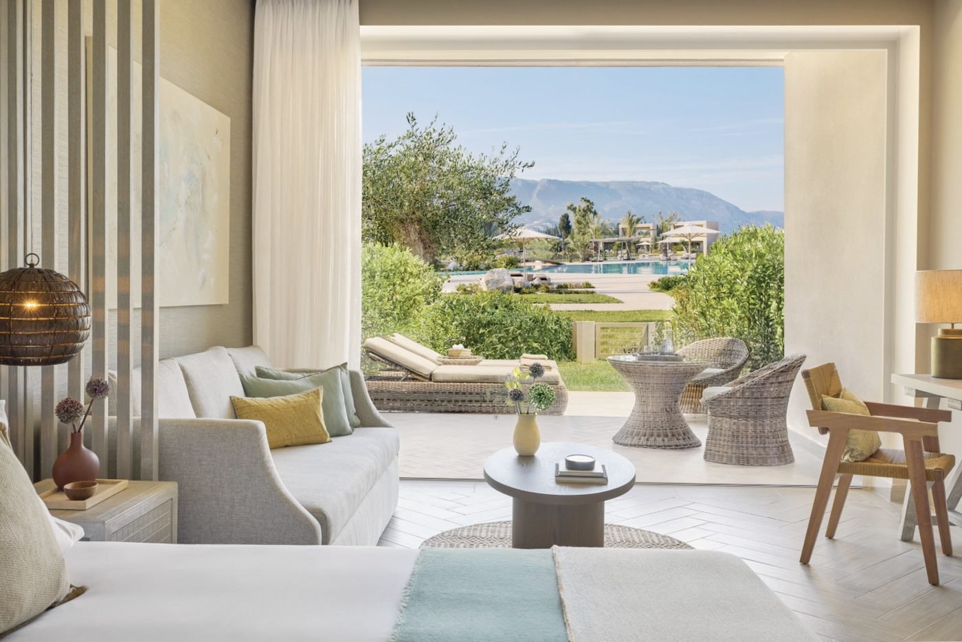 A Junior Suite Private Garden Pool View, its living area opening onto a terrace and garden with the pool and mountains beyond