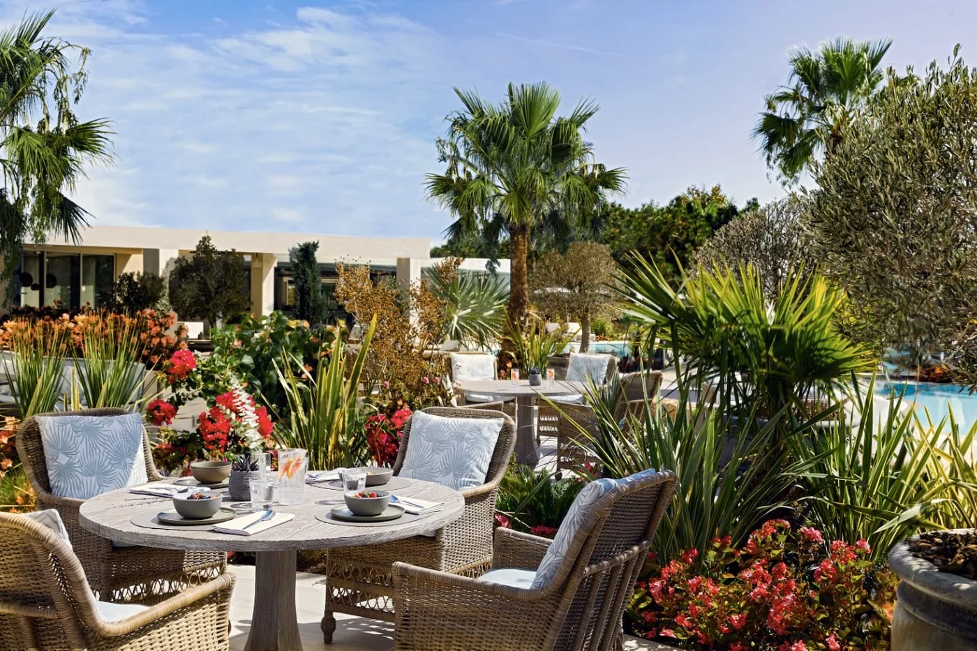 A table set for breakfast on the garden terrace at Artemis, among flowers and palms beside the pool