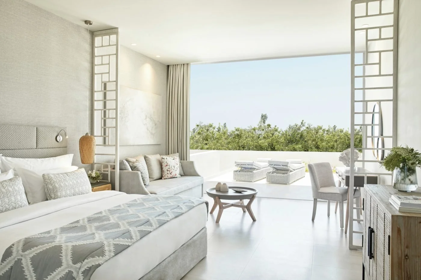 A Junior Suite Private Garden at Ikos Aria with a bed and sofa opening onto a sun terrace with loungers