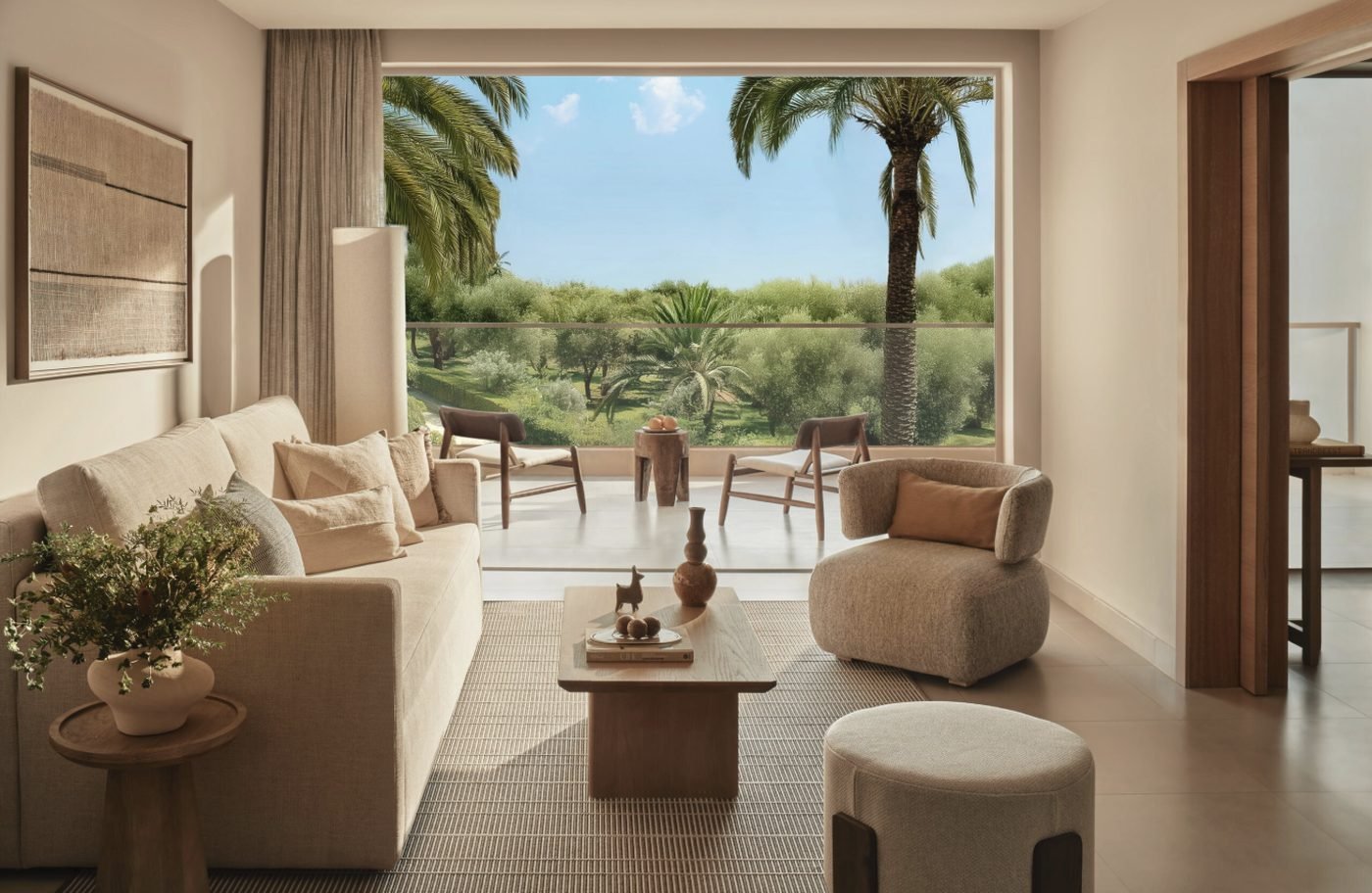 The living room of a One Bedroom Bungalow Suite at Ikos Olivia opening onto a balcony above palm trees and gardens