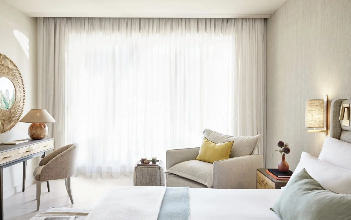 A Double Room at Ikos Odisia with an armchair and desk in front of floor-to-ceiling sheer curtains