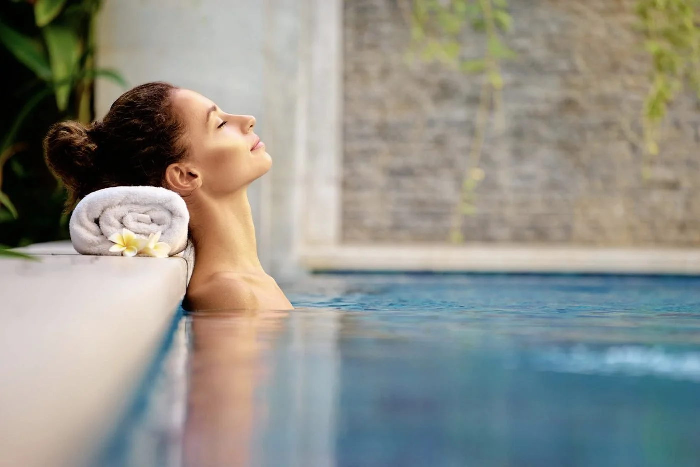 A guest resting her head on a rolled towel at the edge of a spa pool