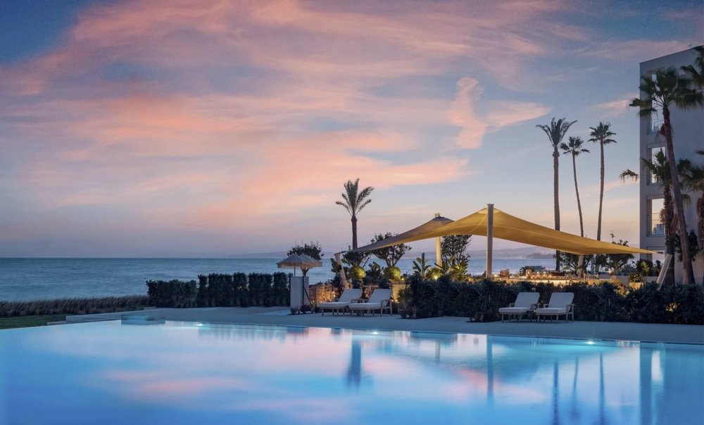 The Deluxe pool at Ikos Andalusia at sunset with palm trees and the sea beyond