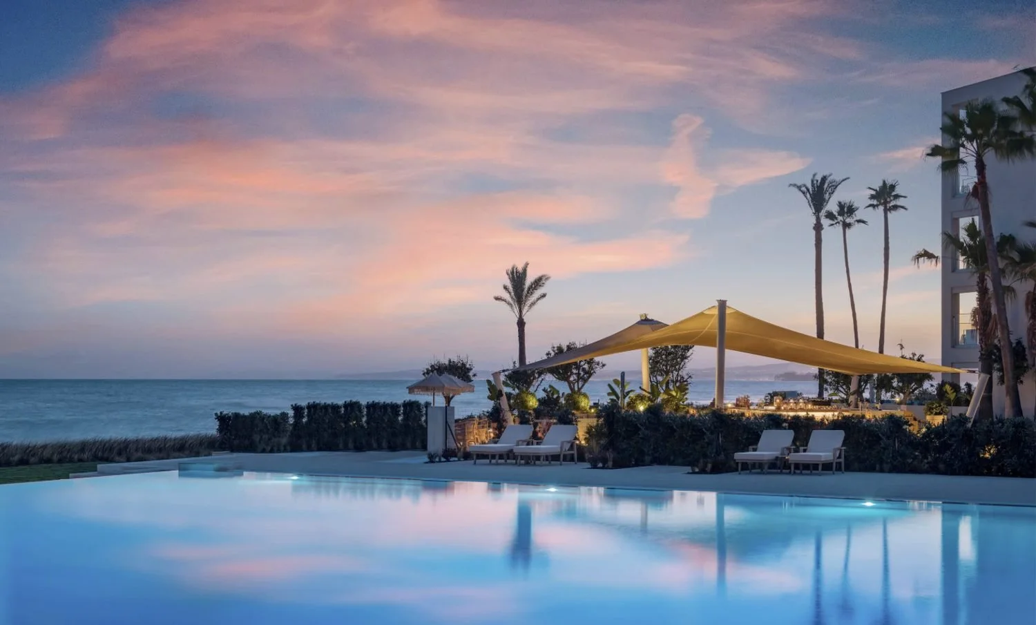 The Deluxe pool at Ikos Andalusia at sunset with palm trees and the sea beyond