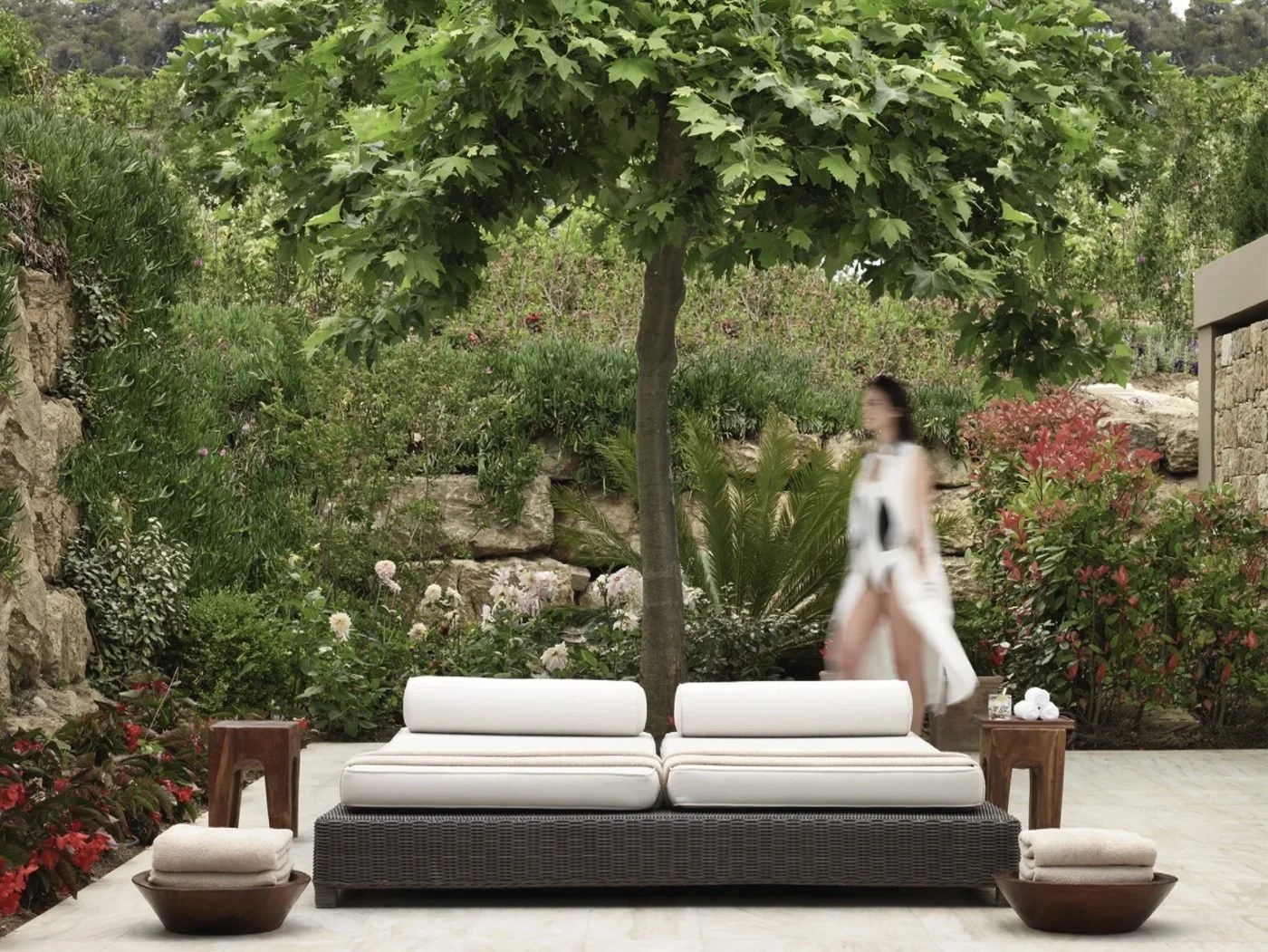 A daybed beneath a plane tree in the garden of the Club Spa, surrounded by flowers and stone walls