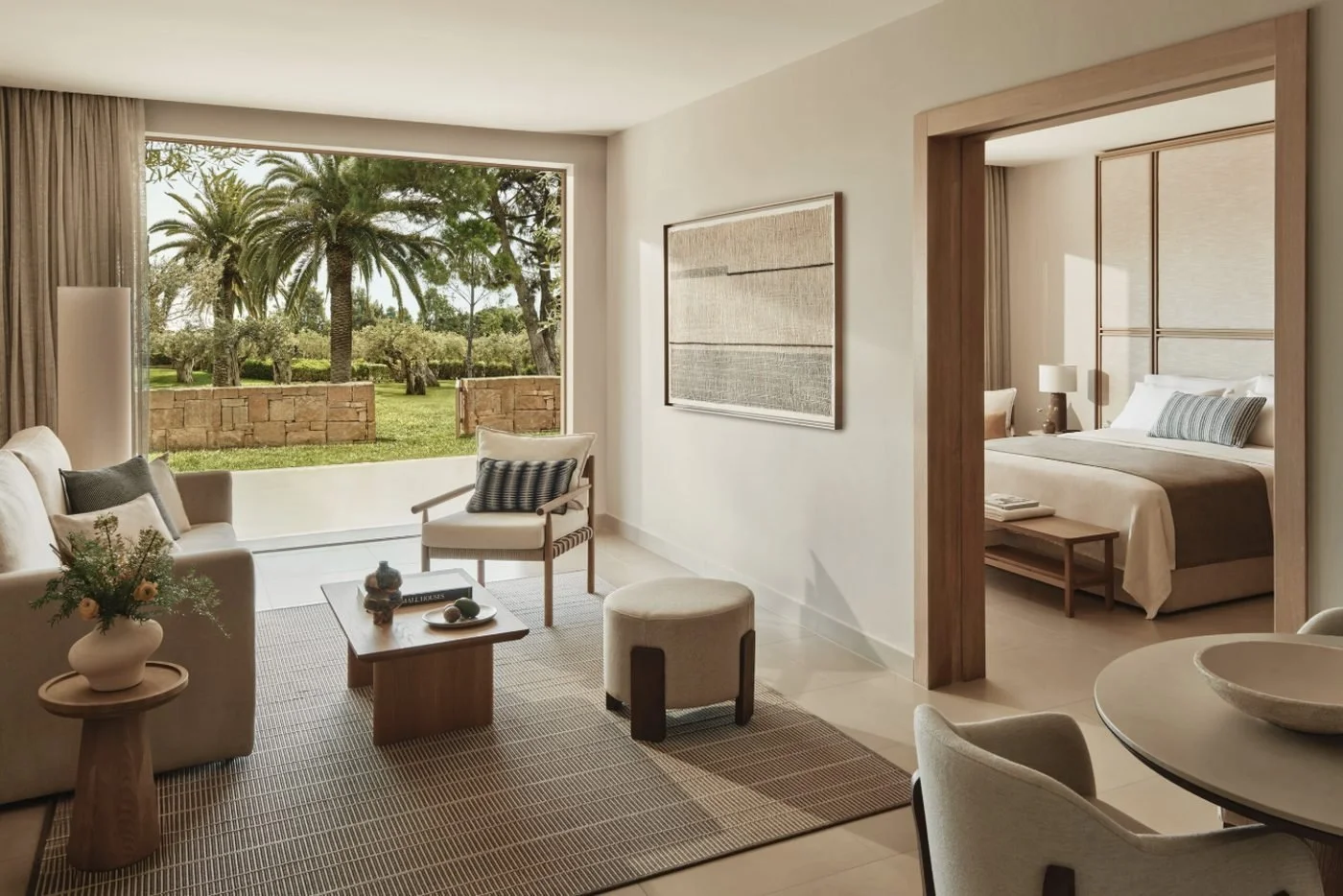 The living room of a Deluxe Two Bedroom Bungalow Suite Private Garden opening onto a lawn with palm trees, with a bedroom beyond