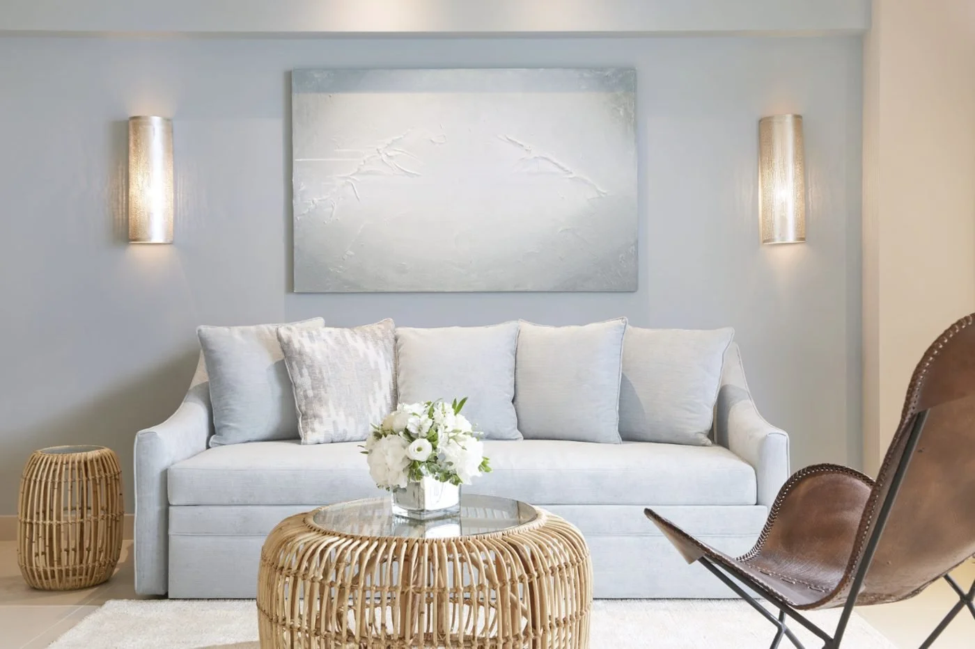The living room of a Deluxe One Bedroom Suite with a pale blue sofa, rattan table and leather sling chair