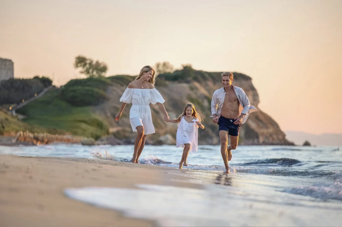 A family running hand in hand along the water's edge at sunset on a Sani beach
