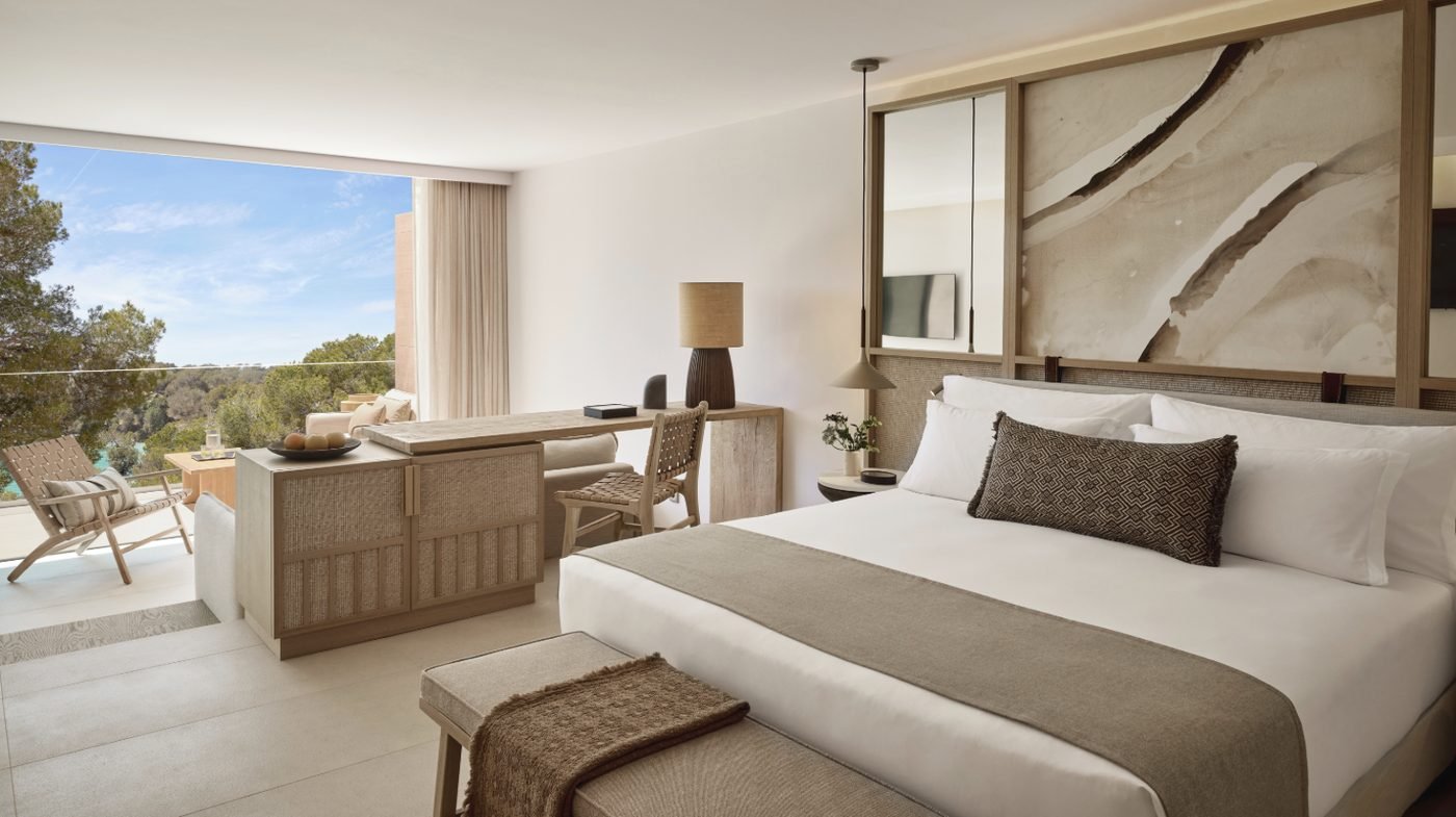 A Deluxe Junior Suite with a bed, desk and sitting area opening onto a balcony among the pines