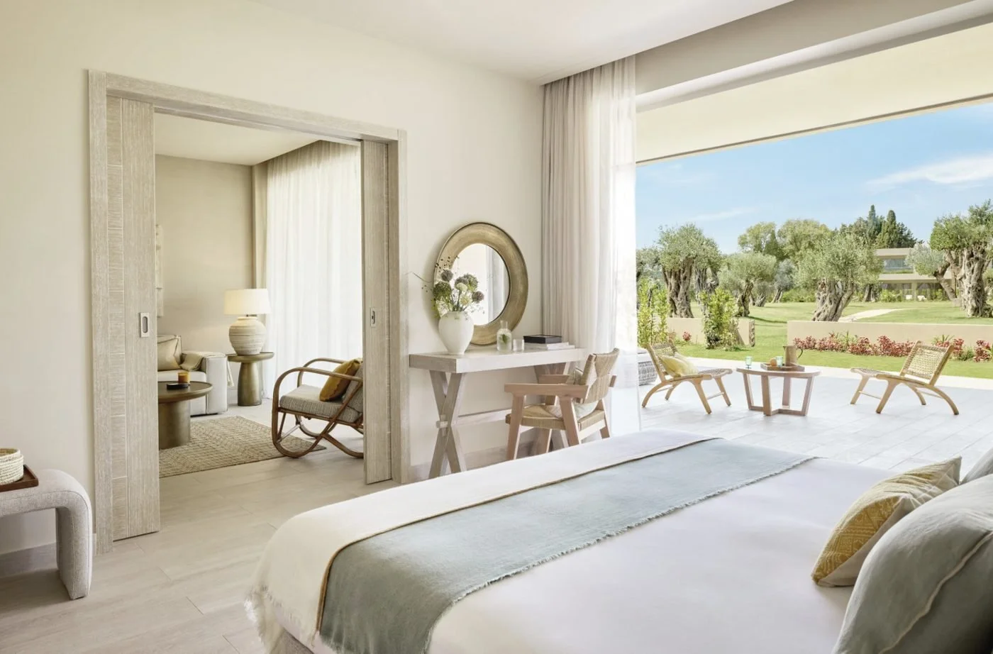 A One Bedroom Suite Private Garden, its bedroom opening onto a terrace and lawn with olive trees, with the living room beyond
