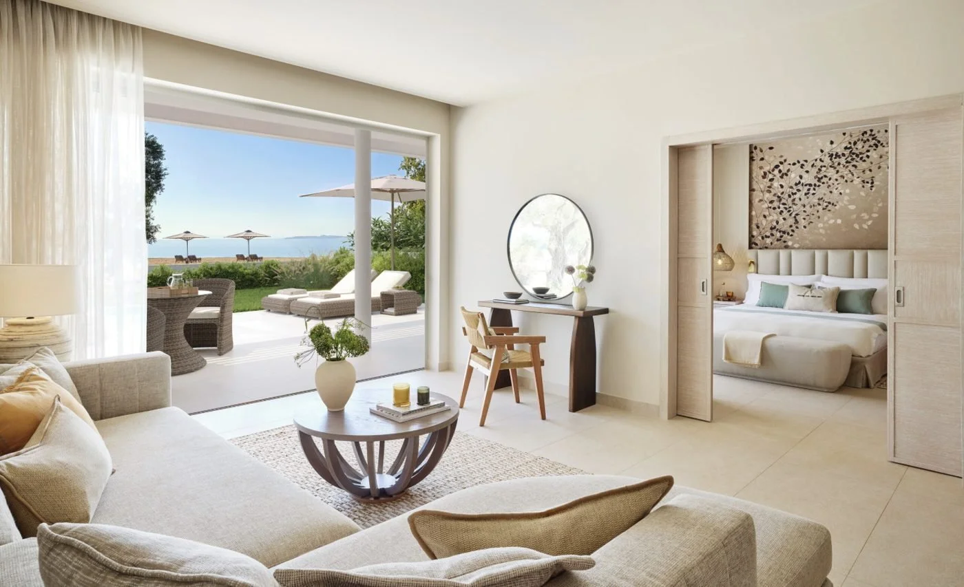 The living room of a Deluxe Two Bedroom Bungalow Suite opening onto a garden terrace and the sea, with a bedroom beyond