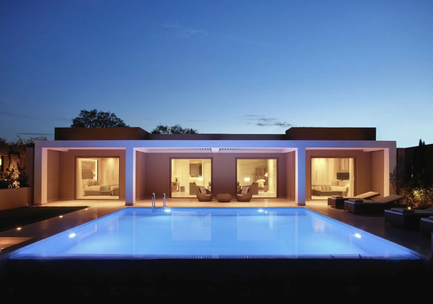 A Deluxe Two Bedroom Bungalow Suite lit up at dusk behind its private pool