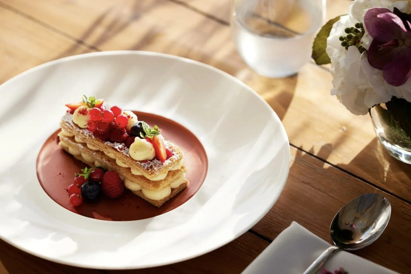 A mille-feuille with fresh berries on a white plate, served on a sunlit table