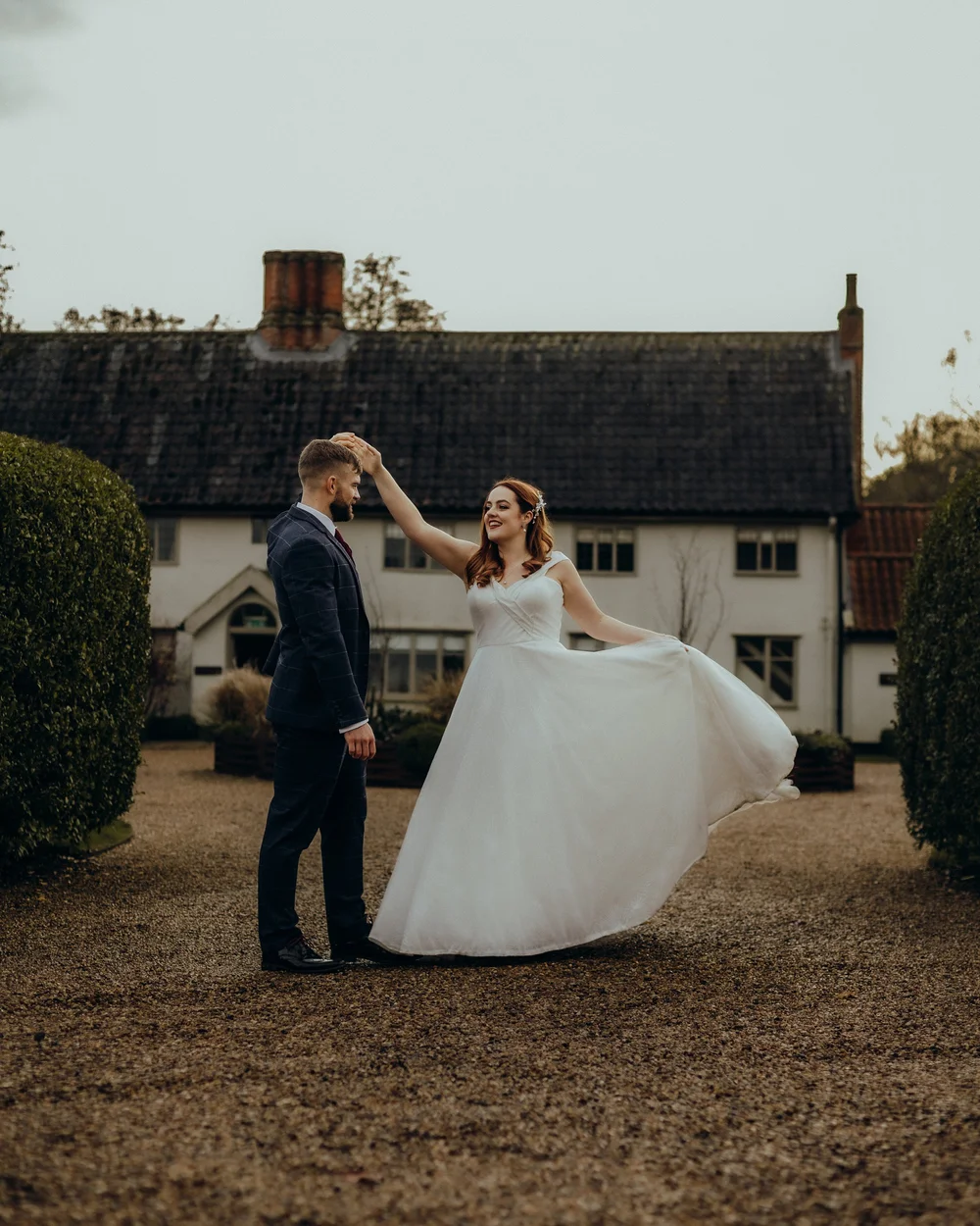 Groom twirling the bride outside a thatched cottage
