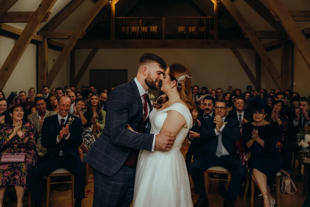 Couple kissing at the end of the aisle as guests applaud