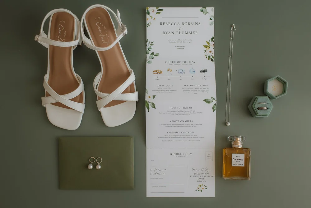 Bridal shoes, invitation and perfume laid out on green