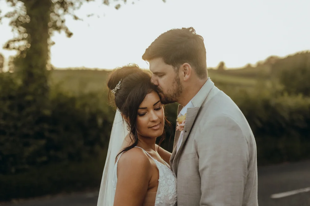 Groom kissing the bride on the forehead at golden hour